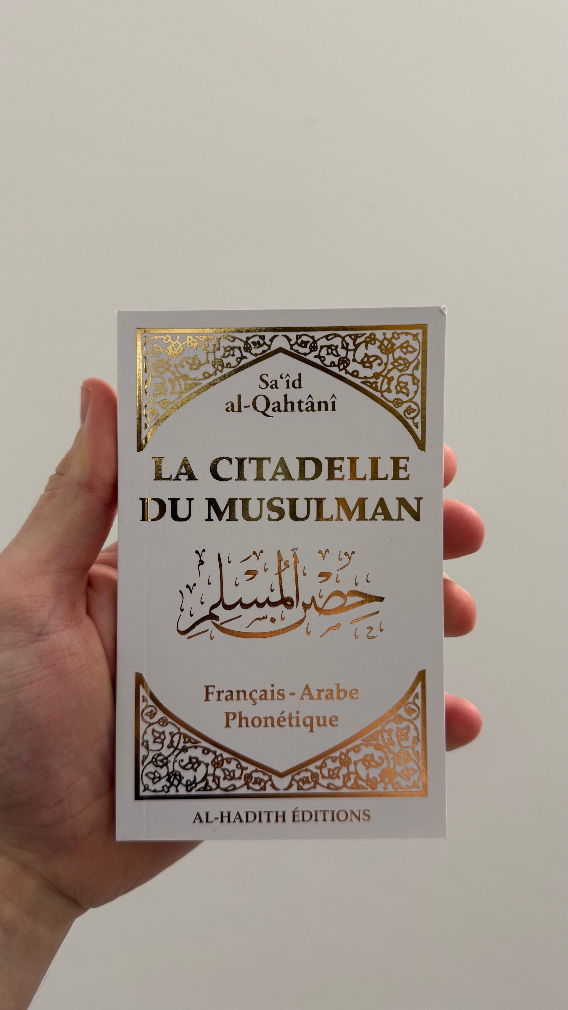 livre blanc avec écriture dorée la citadelle du musulman tenu dans une main