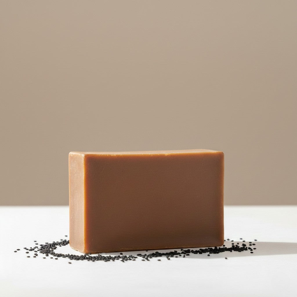Savon à la nigelle naturel et artisanal posé sur un lit de graines de nigelle noires, idéal pour le soin purifiant du visage et du corps.